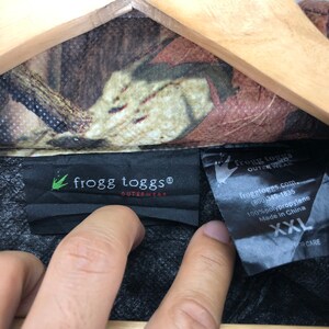 May include: A black and green camouflage jacket with a black label that reads "frogg toggs&reg; OUTERWEAR" and a smaller label that reads "frogg toggs OUTER WEAR froggtoggs.com (800)349-1835 100% polypropylene Made in China XXL OR CARE".