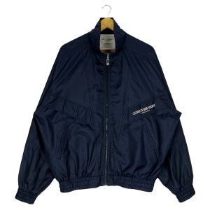 Könnte beinhalten: Eine dunkelblaue Windbreaker-Jacke mit Reißverschluss und geripptem Bund. Die Jacke hat ein "CEIRUTI 1981 SPORT" Logo auf der rechten Brustseite.