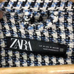 May include: A black and white label with the word "ZARA" in white lettering. The label also includes size information: EUR M, USA M, MEX 28. The label states "MADE IN MOROCCO".