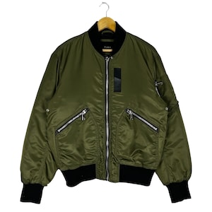 Puede incluir: Una chaqueta bomber verde con ribetes negros y varios bolsillos con cremallera. La chaqueta tiene una cremallera y una etiqueta que dice "ZARA".