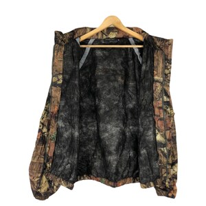 May include: A brown, green, and orange camouflage jacket with a black mesh lining. The jacket has a zipper closure and a hood.