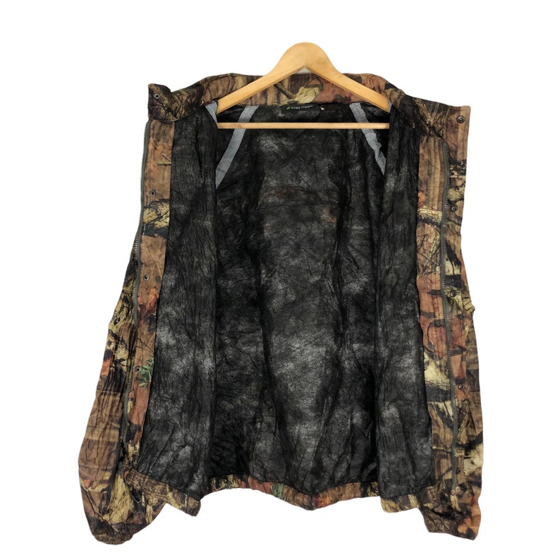 May include: A brown, green, and orange camouflage jacket with a black mesh lining. The jacket has a zipper closure and a hood.