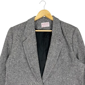 May include: A gray tweed blazer with a black lining. The blazer has a single button closure and a notched lapel.