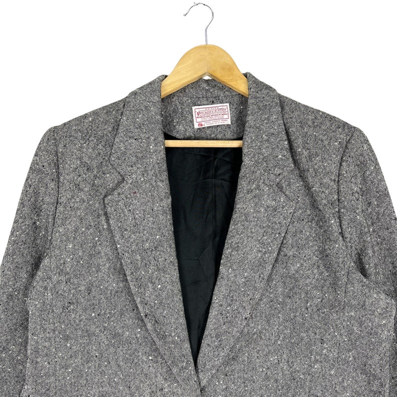 May include: A gray tweed blazer with a black lining. The blazer has a single button closure and a notched lapel.