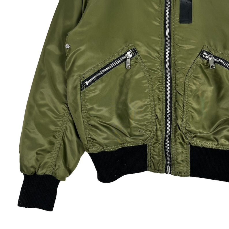 Puede incluir: Una chaqueta bomber verde con detalles de cremallera negra y un cuello, pu&ntilde;os y cintura de punto de canal&eacute; negro.