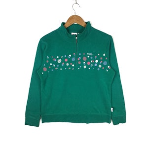 Puede incluir: Sudadera verde de manga larga con cierre de cremallera hasta la mitad y logotipo FILA blanco. La sudadera tiene un patr&oacute;n de lunares de colores.
