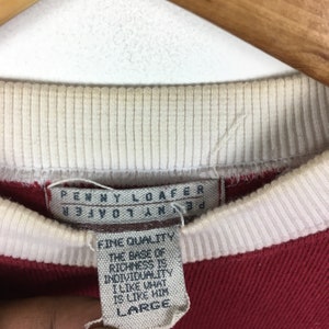 May include: Red and white striped long-sleeve shirt with a white tag that reads "PENNY LOAFER" and "FINE QUALITY THE BASE OF RICHNESS IS INDIVIDUALITY I LIKE WHAT IS LIKE HIM LARGE".