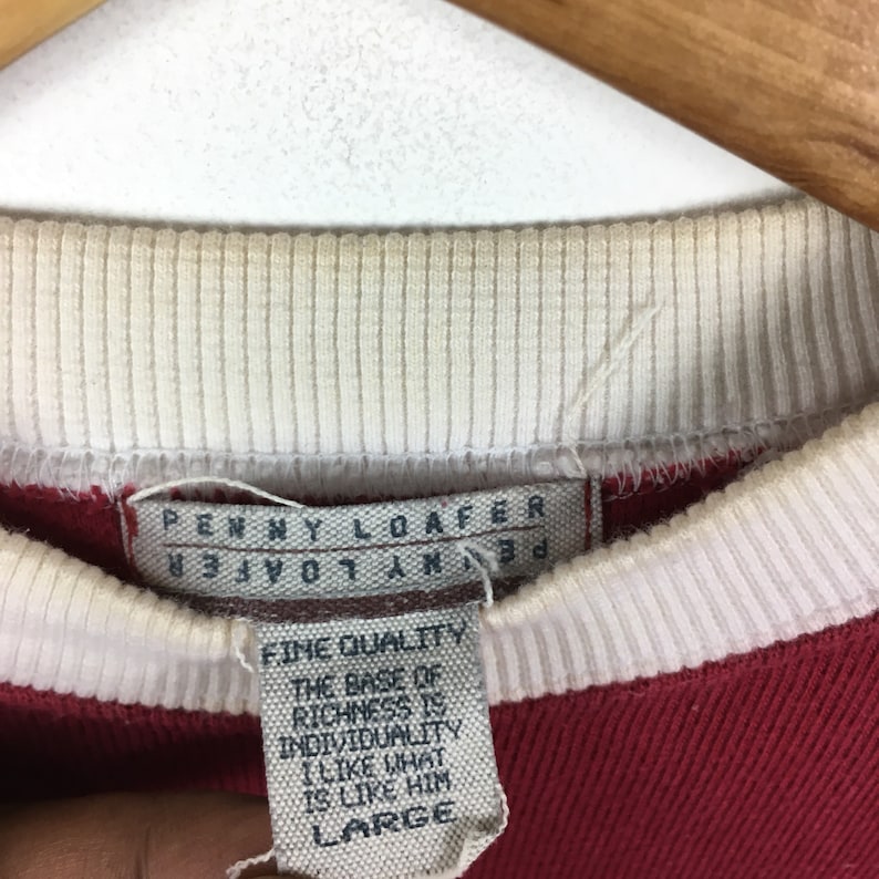 May include: Red and white striped long-sleeve shirt with a white tag that reads "PENNY LOAFER" and "FINE QUALITY THE BASE OF RICHNESS IS INDIVIDUALITY I LIKE WHAT IS LIKE HIM LARGE".