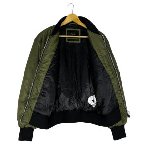 Puede incluir: Una chaqueta bomber verde con cremallera negra y forro negro. La chaqueta tiene una etiqueta que dice "ZARA" en el interior.