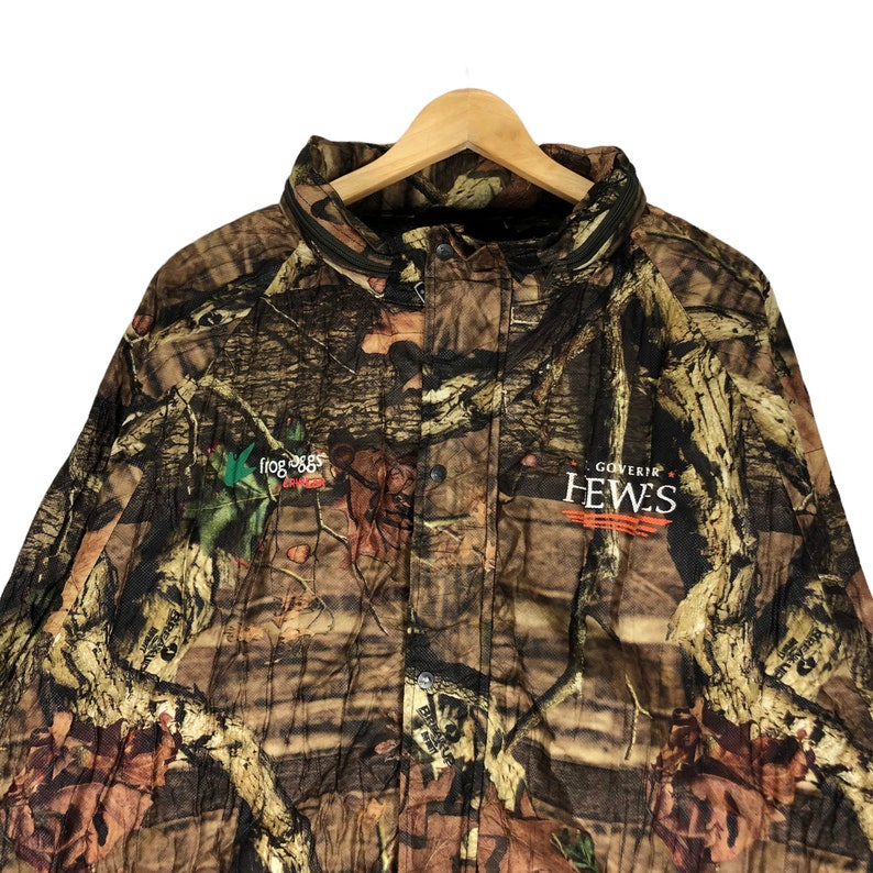 May include: Camouflage jacket with a green frog logo and the text "Goverair Hewes" in white.