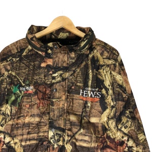 May include: A camouflage jacket with a black zipper and a patch that says "GOVERNOR HEWES" in orange and white text. The jacket also has a green patch with a bird and the text "FROG OGGS" in white.