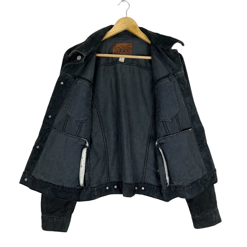 May include: A black denim jacket with a corduroy collar and a brown label that says "Gap" on the inside. The jacket has two pockets on the front and two pockets on the inside.