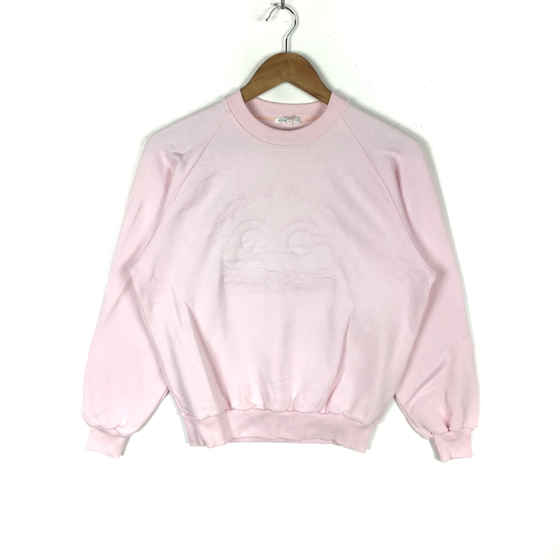 May include: A pink sweatshirt with a white embroidered logo that says "Champion" and "Authentic Athletic Apparel".