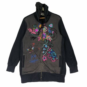 Peut inclure: Un sweat à capuche noir et gris avec une fermeture éclair, orné d'un motif floral coloré et d'un visage de femme sur le devant. Le motif comprend des papillons, des fleurs et des bijoux. Le texte "Ro Sham" est imprimé sur le devant.