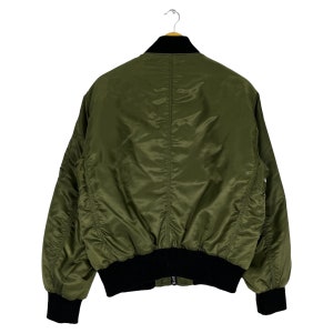 Puede incluir: Una chaqueta bomber verde oscuro con cuello y pu&ntilde;os de canal&eacute; negros. La chaqueta tiene cierre de cremallera y dos bolsillos en la parte delantera.