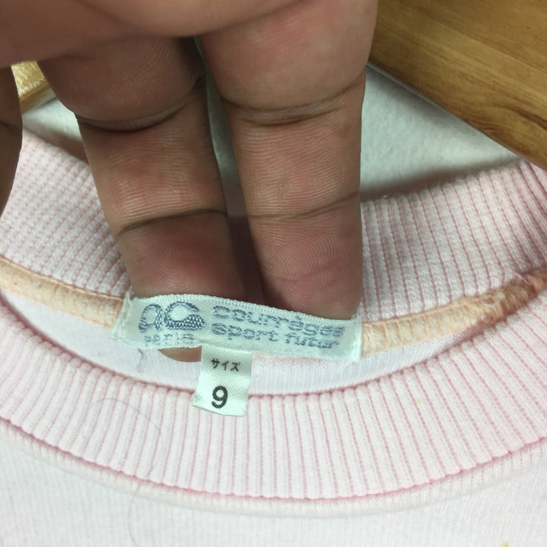 May include: Pink sweatshirt with a white tag that says "Courreges Sport Futur Paris" and a size tag that says "Size 9".