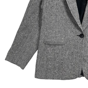 May include: A gray tweed blazer with a single button closure and a pocket on the left side.