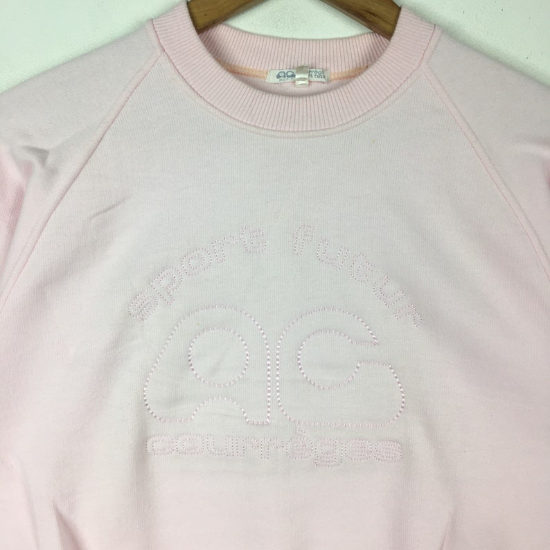 May include: A pink sweatshirt with a white embroidered logo that says "Sporty Fashion" and "AC" in a stylized font.