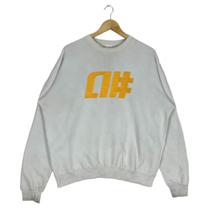 Könnte beinhalten: Ein weißer Pullover mit einem großen orangenen Aufdruck der Buchstaben "D" und "#" auf der Vorderseite.