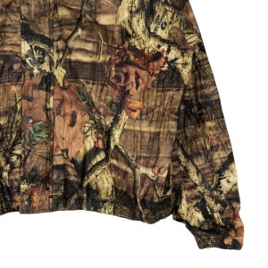 May include: A brown, green, and beige camouflage jacket with a button-up front closure. The jacket has a relaxed fit and a slightly cropped length.