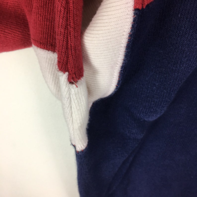 May include: Close-up of a red, white, and navy blue sweater. The sweater is made of a soft, knitted fabric. The seams are visible at the edges of the different colored panels.