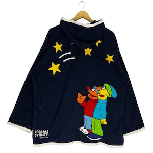 May include: A navy blue hooded sweatshirt with a Sesame Street graphic. The graphic features Big Bird and Elmo looking up at a starry night sky. The text "Sesame Street" is printed on the bottom left corner of the sweatshirt.