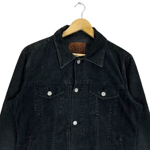 May include: A black corduroy jacket with a button closure and two chest pockets. The jacket has a brown leather label with the text "the gap" on the left side of the chest.