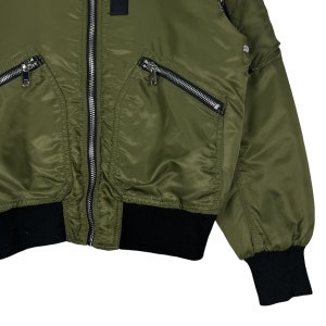 Puede incluir: Una chaqueta bomber verde con pu&ntilde;os y cintura de canal&eacute; negros. La chaqueta tiene cierre de cremallera y varios bolsillos con cierre de cremallera.