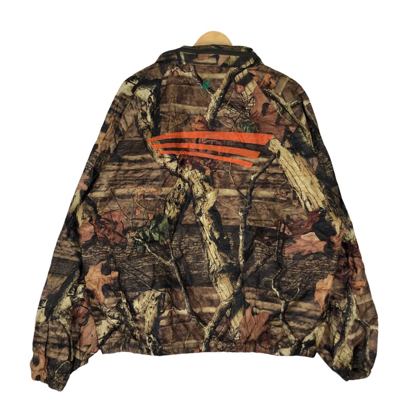 May include: A brown and green camouflage jacket with an orange stripe across the back. The jacket has a zipper closure and a stand-up collar.