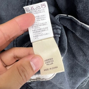 May include: A white tag with black text attached to a dark gray garment. The tag contains washing instructions in Japanese and the following information: s/668365 v/305753 FALL09 MADE IN CHINA