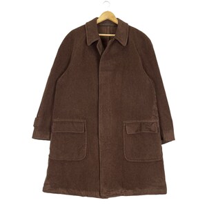 May include: A brown corduroy coat with a collared neckline, two large front pockets, and long sleeves. The coat is hanging on a wooden hanger. The coat is a medium length.