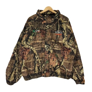 May include: Camouflage jacket with a brown, green, and orange pattern. The jacket has a zipper closure and a button-up flap. The text "GORDON HEWES" is printed on the front of the jacket.