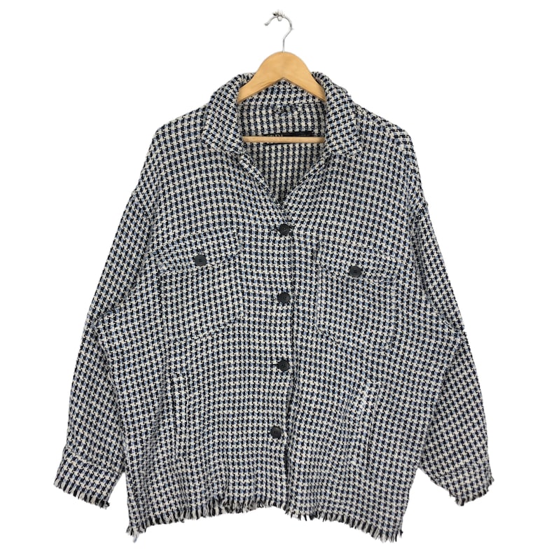 May include: A black and white checkered button-up shirt with frayed edges. The shirt has two flap pockets on the front and a button closure.