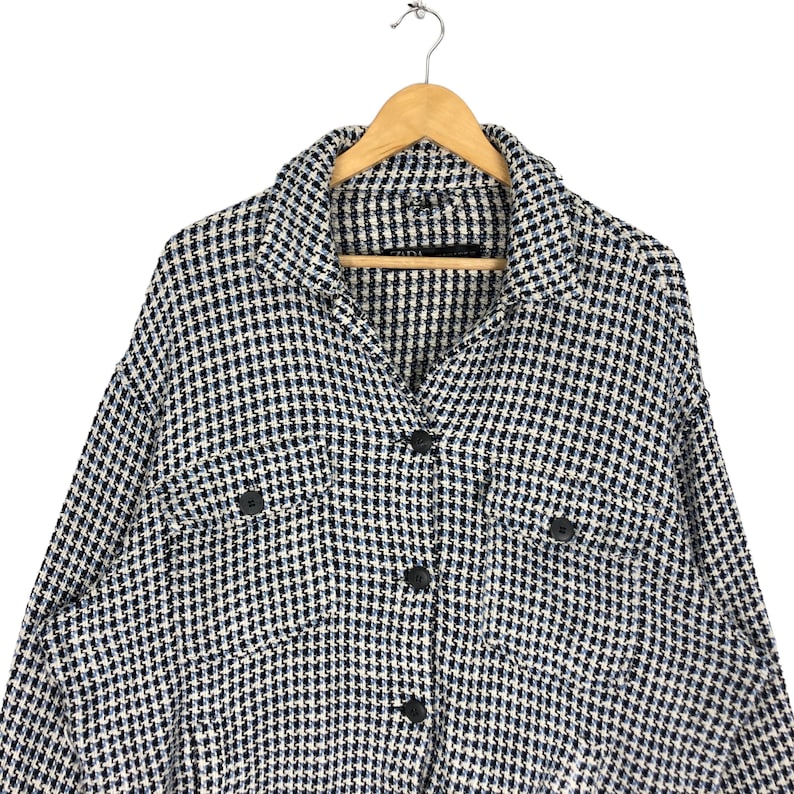 May include: A white and blue checkered button-up shirt with long sleeves and two flap pockets. The shirt has a collared neckline and a button closure.