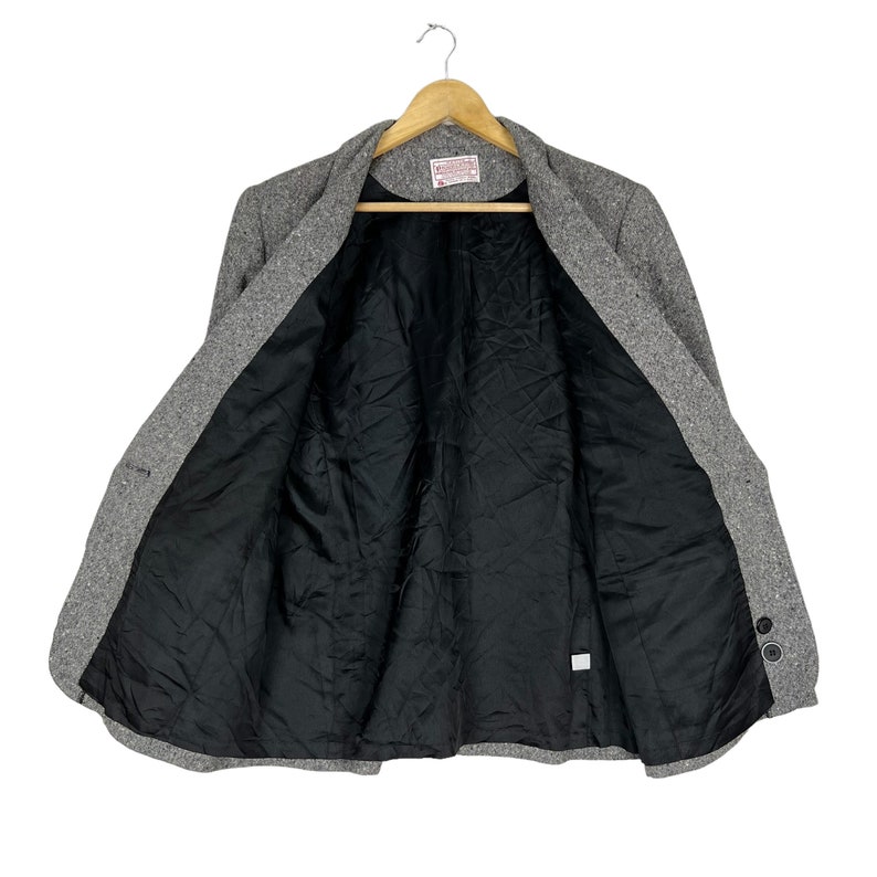 May include: A gray tweed blazer with a black lining. The blazer has a single button closure and two pockets on the front.