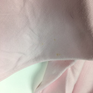 May include: A close-up of a pale pink fabric with a few small yellow stains.