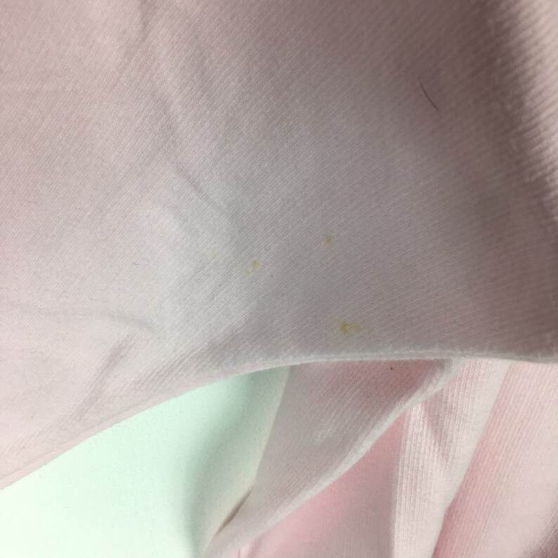 May include: A close-up of a pale pink fabric with a few small yellow stains.