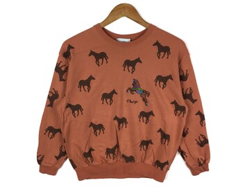 May include: A brown sweatshirt with a horse print all over. The sweatshirt has a colorful horse design on the front with the word "Charge" underneath.