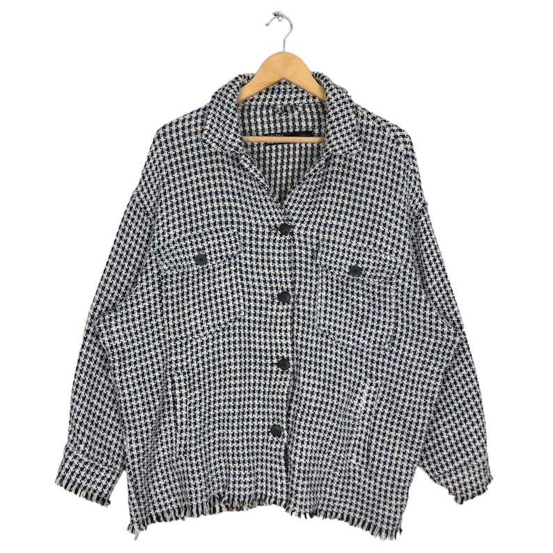 May include: A black and white checkered button-up shirt with a frayed hem. The shirt has two flap pockets on the front and is hanging on a wooden hanger.