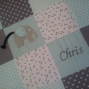 Könnte beinhalten: Eine Babydecke mit Patchwork-Muster in hellblau, grau und weiß. Die Decke hat eine Filz-Elefanten-Applikation und den Namen "Chris" bestickt.