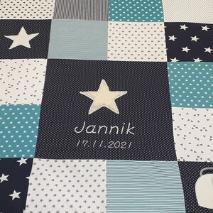 Könnte beinhalten: Eine blaue und weiße Patchwork-Babydecke mit einem weißen Stern und dem Namen "Jannick", der in der Mitte gestickt ist. Das Datum "17.11.2021" ist ebenfalls unter dem Namen gestickt.