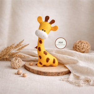 May include: A handmade yellow felt giraffe with brown spots, a white muzzle, and brown ears. The giraffe is displayed on a wooden slice with small wooden beads and a ball of twine. A PDF sewing pattern is indicated in the image.