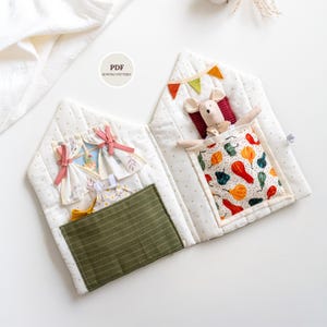 May include: A handmade fabric house-shaped quiet book with a mouse toy. The book features a green pocket, a window with curtains, and a bed with a colorful patterned blanket. The cover has the text "PDF Sewing Pattern".