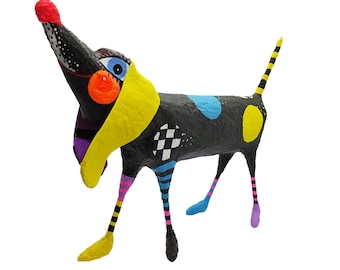Può includere: Una scultura di cane in cartapesta nera, gialla, blu e rosa con un design fantasioso. Il cane ha un muso lungo, occhi grandi e un collare giallo.