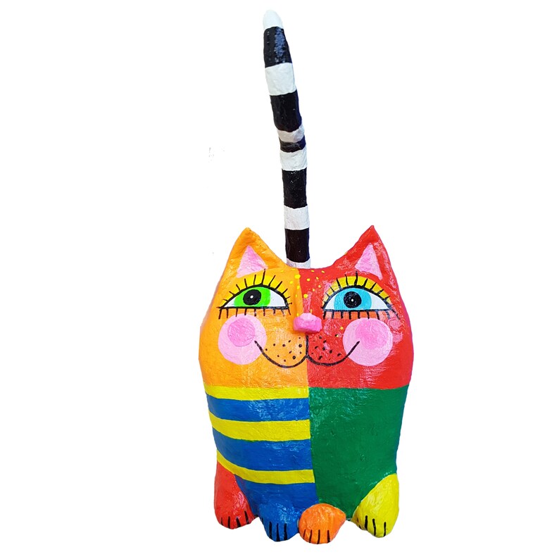 Eine farbenfrohe Katzenskulptur. Die Katze ist in Abschnitte aus Orange, Gelb, Rot, Grün und Blau unterteilt. Sie hat einen gestreiften Schwanz und große, ausdrucksstarke Augen. Ein einzigartiges Stück Volkskunst.