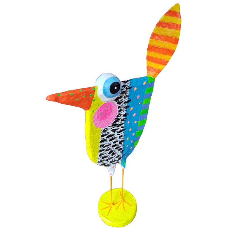 Faszinierende Dreiviertel-Ansicht von oben auf die Vogel Figur aus Pappmaché, die die plastische, handwerkliche Textur der moderne naive Kunst Skulptur betont. Der Fantasievogel steht auf grazilen orangefarbenen Beinen auf einem leuchtend gelben Sockel. Sichtbar sind der gepunktete Schnabel, die markante rosa Wange auf gelbem Grund sowie das aufwendige schwarz-weiße Federmuster und die Punkte auf blauem Grund. Ein einzigartiges Kunst-Unikat als Blickfang.