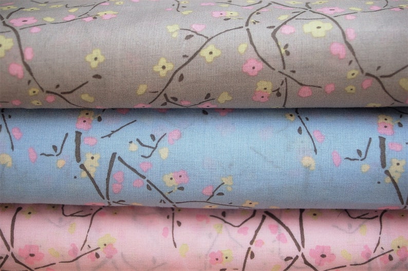 May include: Three fabric swatches with a floral pattern. The top swatch is gray with pink and yellow flowers. The middle swatch is light blue with pink and yellow flowers. The bottom swatch is pink with pink and yellow flowers.