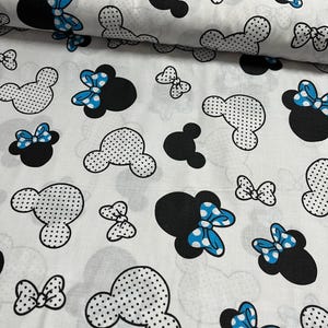 Könnte beinhalten: Weißer Stoff mit einem sich wiederholenden Muster aus schwarzen und weißen gepunkteten Mickey-Maus-Köpfen mit blauen Schleifen. Die Schleifen haben weiße Punkte.