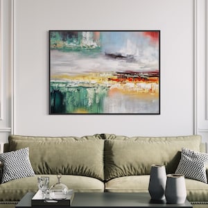 Peut inclure: Peinture abstraite aux couleurs vert, jaune, orange et rouge. La peinture est encadrée de noir et est accrochée à un mur blanc au-dessus d'un canapé vert.
