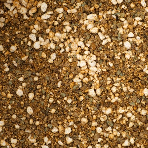 May include: Close-up of a mixture of small brown, white, and green pebbles. The pebbles are arranged in a random pattern and create a textured surface.